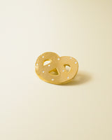Shiny gold-colored hard enamel pin with metal butterfly clasp in the form of a pretzel cookie.