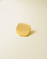 Shiny gold-colored hard enamel pin with metal butterfly clasp in the form of an irregular tea biscuit.