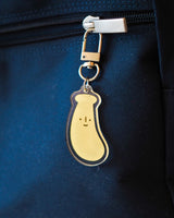 Banana with a cute smile acrylic keychain attached to a key displayed on the zipper of a blue backpack