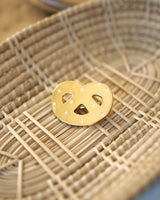 Shiny gold-colored hard enamel pin with metal butterfly clasp in the form of a pretzel cookie displayed in a basket.