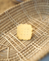 Shiny gold-colored hard enamel pin with metal butterfly clasp in the form of an irregular tea biscuit displayed in a basket.