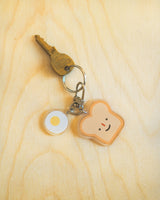 Bread and egg with a cute smile acrylic keychain attached to a key displayed on a wooden surface