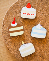 A set of all 4 different wooden cake magnets on a cork surface