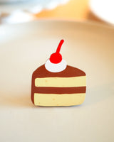 Chocolate cake slice with a cherry on top wooden magnet displayed on a plate
