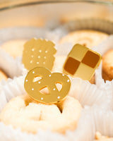 Set of all 3 different Shiny gold-colored hard enamel pins displayed in a tray of cookies