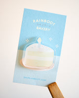 Birthday cake slice with sprinkles acrylic magnet displayed with a blue backing card on a white background.